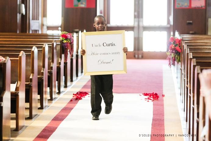 Boys walks down aisle with sign at wedding